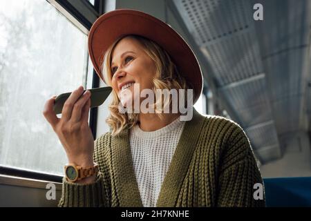Donna sorridente che invia messaggi vocali tramite smartphone in treno Foto Stock