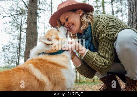 Cane che lecca faccia di donna accovacciata nella foresta Foto Stock