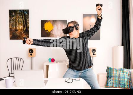 Uomo allegro che indossa simulatore di realtà virtuale puntando mentre si trova a tavola Foto Stock