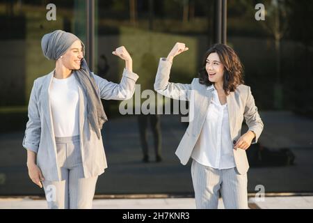 Donna d'affari fiduciosa con le braccia incrociate in piedi da una collega di fronte al muro di vetro Foto Stock