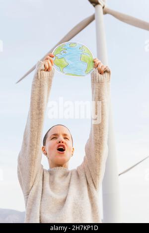 Donna che grida mentre tiene terra che disegna alla turbina eolica Foto Stock