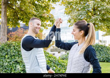 Uomo e donna sorridenti che controllano il orologio da polso al parco Foto Stock