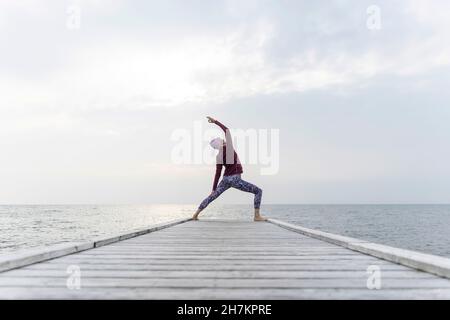 Donna che pratica Utthita Parsvakonasana posa sul molo Foto Stock