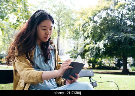 Giovane donna che si concentra mentre scrive in diario al parco Foto Stock