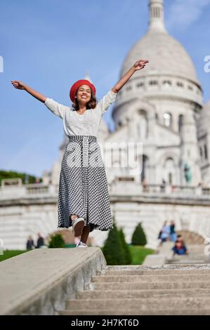 Donna sorridente con le braccia distese in piedi a Basilique Du Sacre Coeur, Montmartre a Parigi, Francia Foto Stock