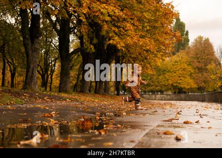 Ragazzo con impermeabile marrone che gioca nel parco autunnale Foto Stock