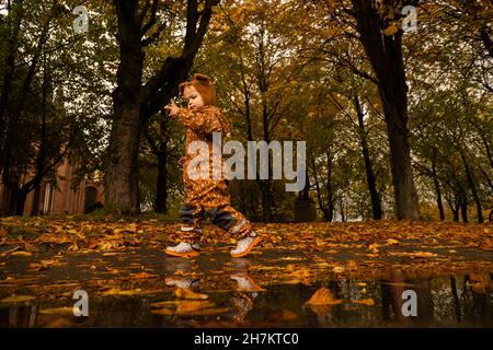 Ragazzo con impermeabile marrone che cammina nel parco autunnale Foto Stock