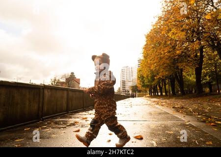 Toddler che indossa un impermeabile che cammina su strada Foto Stock