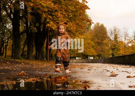 Ragazzo carino che indossa un impermeabile che corre su strada nel parco Foto Stock