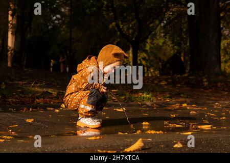 Ragazzo con impermeabile marrone e cappellino che gioca alla pozzanghera Foto Stock