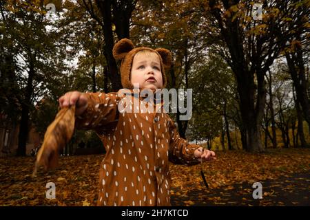 Ragazzo con impermeabile marrone che gioca con la foglia nel parco Foto Stock