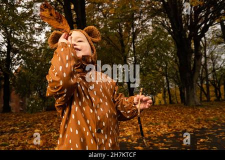 Ragazzo con impermeabile marrone e cappello che gioca nel parco Foto Stock