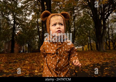 Ragazzo carino con impermeabile marrone e cappellino al parco autunnale Foto Stock