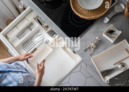 Primo piano le mani femminili montando ordinatamente le posate in scatole di stoccaggio pp a cassetto della cucina minimalista Foto Stock