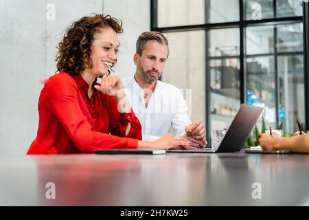 Donna d'affari sorridente che usa il laptop mentre lavora con i colleghi in ufficio Foto Stock