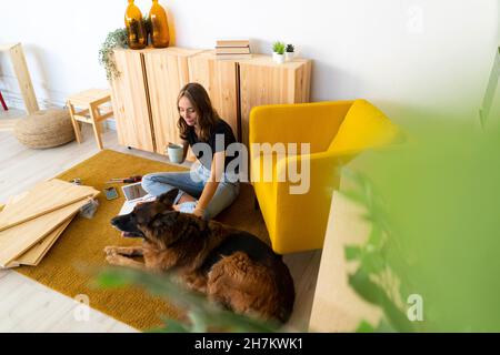 Donna sorridente con cane che ha un caffè in soggiorno Foto Stock