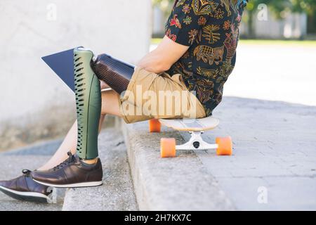 Uomo disabili sorridente con capelli lunghi utilizzando un computer portatile nel parco pubblico Foto Stock