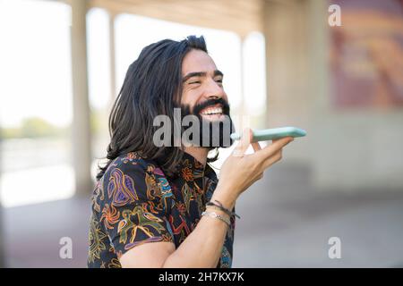 Happy hipster uomo con cuffie che tengono occhiali in parco Foto Stock
