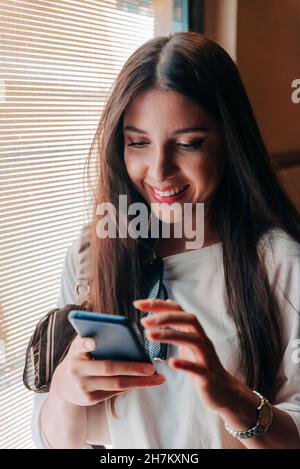 Donna che utilizza il telefono cellulare vicino a finestra Foto Stock
