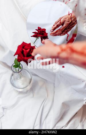 Donna che tocca la rosa con mano sanguinante da riflesso specchio Foto Stock