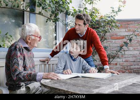 Uomo e ragazzo sorridenti che guardano il padre anziano che parla nel cortile Foto Stock