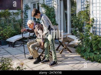 Ragazzo aiutando nonno a levarsi in piedi in su nel cortile Foto Stock