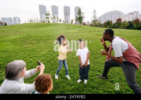 Donna che scatta foto della famiglia attraverso il telefono cellulare nel parco Foto Stock