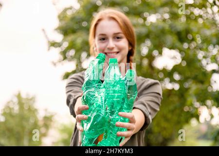 Sorridente volontario femmina che mostra bottiglie di plastica verde in giardino Foto Stock