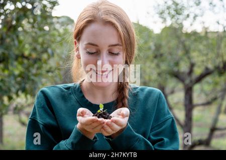 Bella donna contadina con le mani cucito tenendo pianta in giardino Foto Stock
