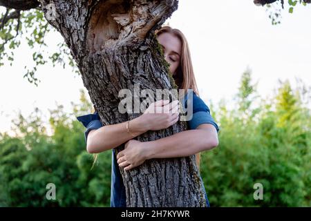 Giovane donna con occhi chiusi abbracciando l'albero Foto Stock