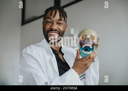 Giovane medico allegro che tiene anatomico modello del cranio umano in ufficio Foto Stock