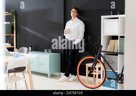 Pensò uomo d'affari con una tazza di caffè appoggiata sulla parete nera in ufficio Foto Stock