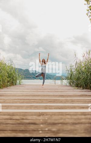Donna con le braccia sollevate facendo yoga sul molo Foto Stock