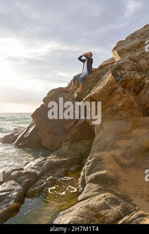 Uomo seduto su roccia gridando in spiaggia Foto Stock