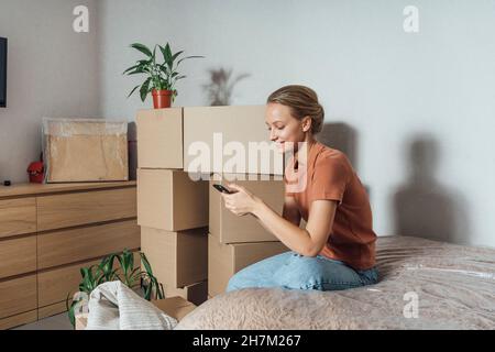 Giovane donna che usa il telefono cellulare sul letto avvolto in plastica Foto Stock