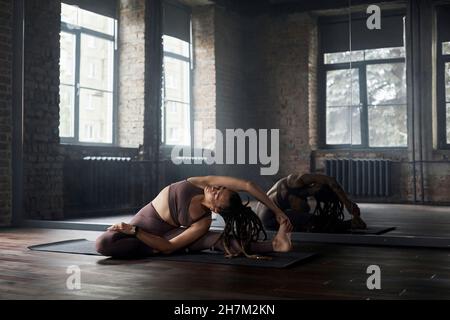 Giovane donna sportiva che fa esercizio di stretching davanti allo specchio in palestra Foto Stock