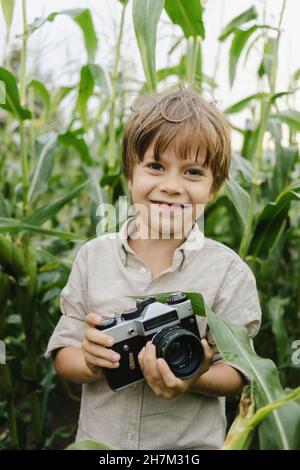 Ragazzo sorridente che tiene la macchina fotografica in campo di mais Foto Stock