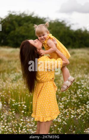 Madre che tiene aloft e bacia la figlia sul prato Foto Stock