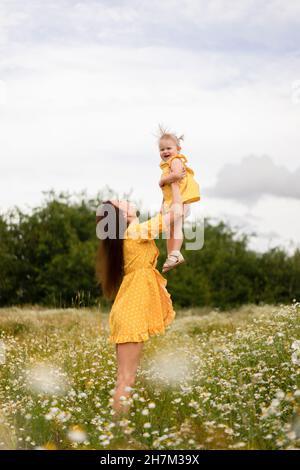 Madre giocosa che tiene la figlia aloft in mezzo ai fiori sul prato Foto Stock