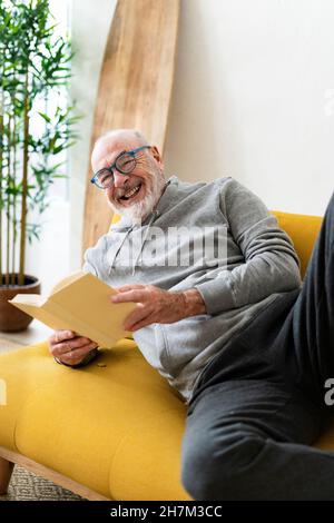 Uomo anziano che legge libro e riposa sul divano a casa Foto Stock