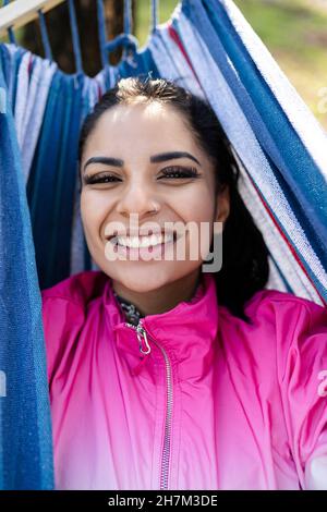 Una mano donna che tiene lo smartphone in videochiamata rilassarsi in amaca al parco Foto Stock