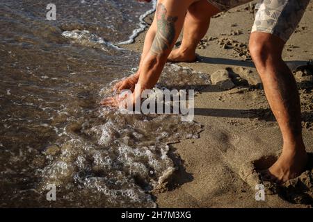 foto di qualcuno che ha un tatuaggio in mano giocando in acqua sulla spiaggia Foto Stock