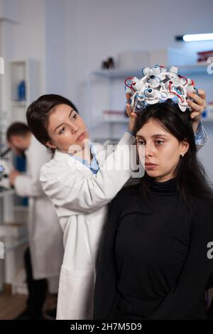 Ricercatore ingegnere donna mettere lo scanner eeg sulla testa della paziente durante l'esperimento di neurologia in laboratorio medico. Medico neurologo analisi dell'evoluzione cerebrale monitoraggio dell'attività del sistema nervoso Foto Stock