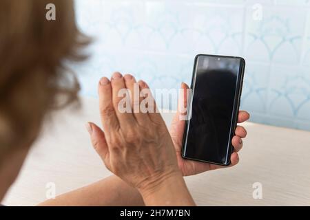 Donna anziana con occhiali che tengono uno smartphone. Nonna è al telefono. Un uomo anziano guarda uno schermo del telefono vuoto. Una schermata vuota per il test e d Foto Stock