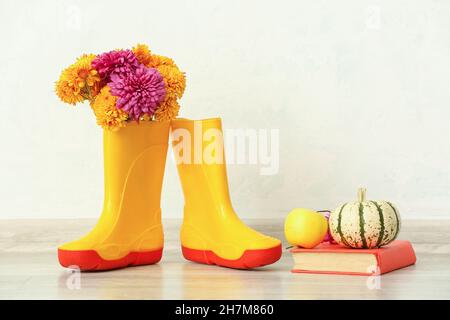 Composizione con stivali in gomma, fiori e libro contro la parete di luce Foto Stock