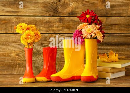 Stivali di gomma, fiori e libri su sfondo di legno Foto Stock