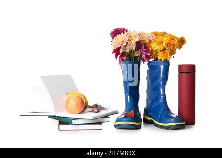 Stivali in gomma, thermos, libri e frutta su sfondo bianco Foto Stock