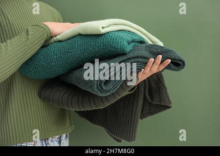 Donna che tiene stack di maglioni caldi su sfondo verde Foto Stock