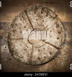 Pagnotta piatta rotonda di pane di segale con un foro al centro su una tavola di legno con briciole di pane Foto Stock