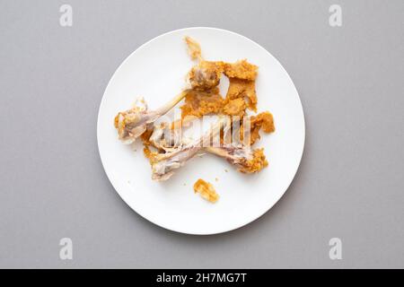 Cibo disordinato rimasto, ossa di pollo come fast food sulla piastra bianca in ceramica, vista dall'alto Foto Stock